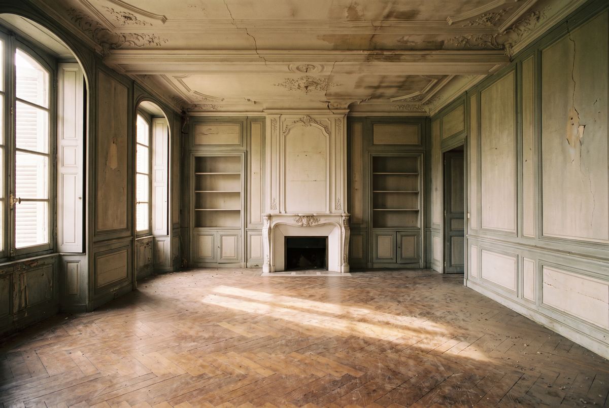Grande pièce lambrissée d’un manoir ancien, parquet usé et cheminée en marbre