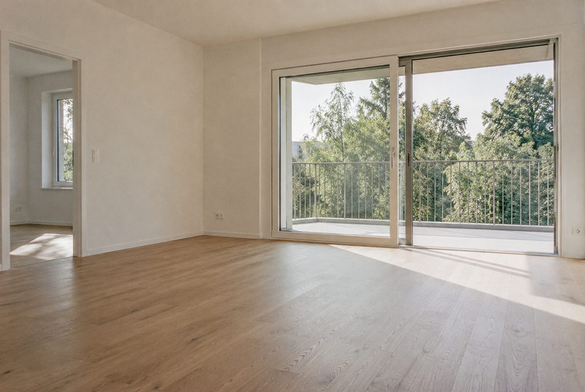 Séjour vide d’un appartement neuf, parquet clair et baie vitrée ouverte sur un balcon